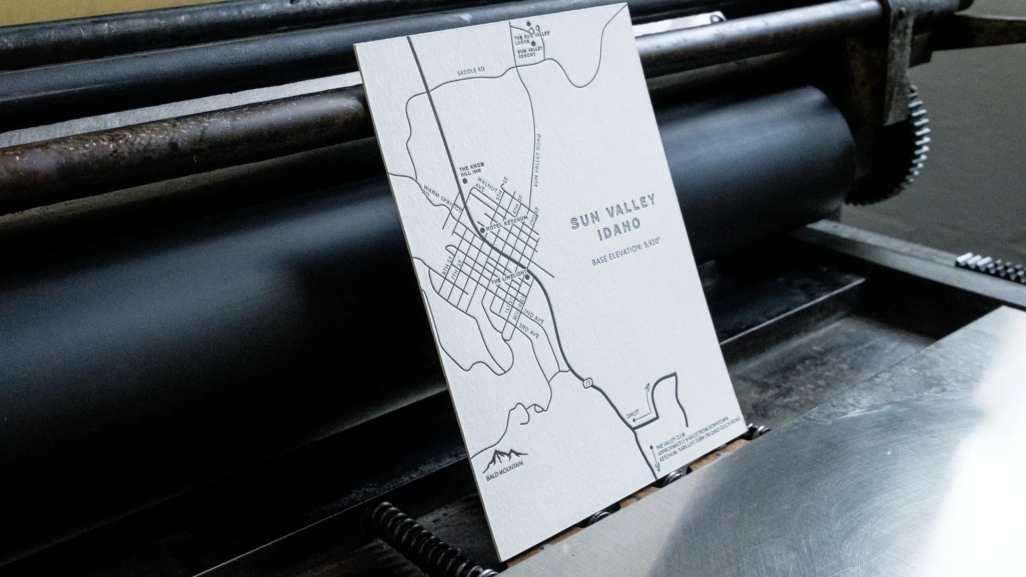 A letterpress-printed map card resting on the inked cylinder of a press